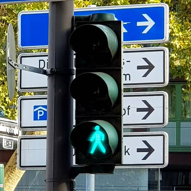 Eine normale Ampel leuchtet grün. Im Hintergrund sind mehrere Schilder zu sehen.