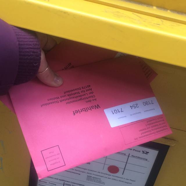 Ein rosa Briefumschlag wird in den Briefwahl gesteckt. Hier wird Briefwahl gemacht.