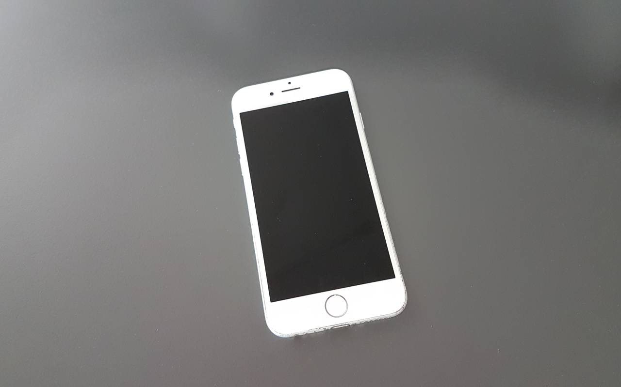 Ein weißes Handy liegt auf einer grauen Platte. Es ist ein frühes I-Phone.