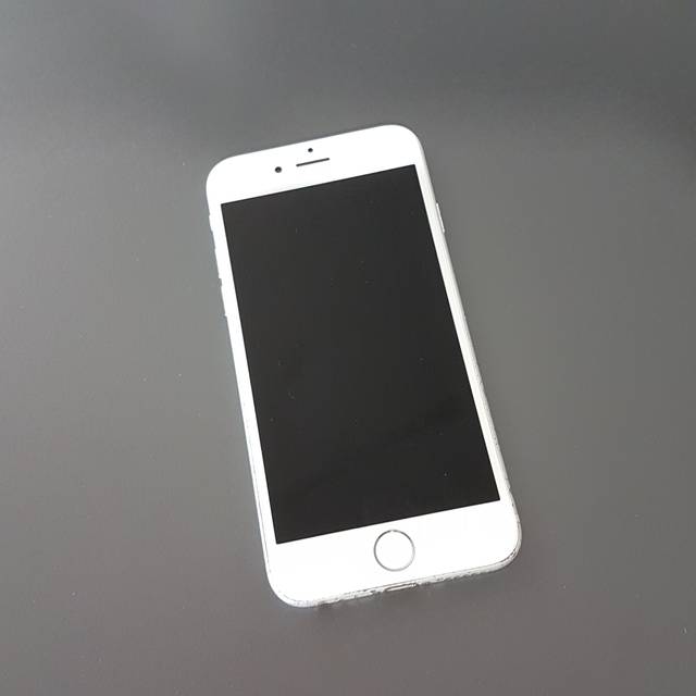 Ein weißes Handy liegt auf einer grauen Platte. Es ist ein frühes I-Phone.