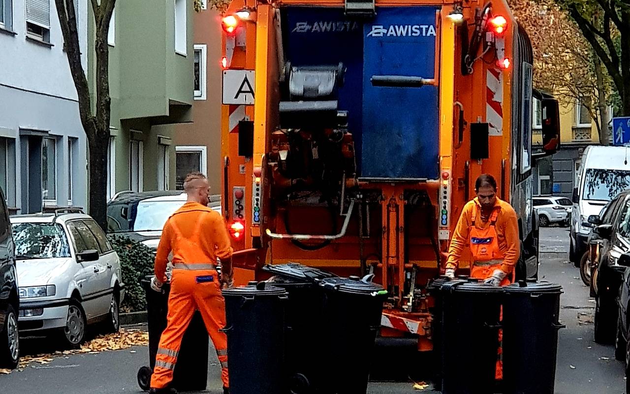 Zwei Mitarbeiter der Awista heben Mülltonnen in einem Müllwagen.