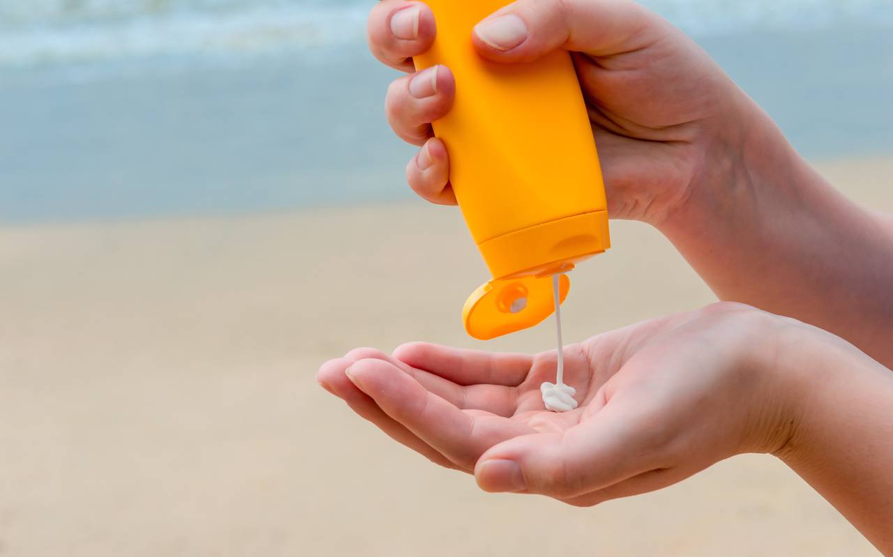 Sonnencreme wird aus einer Flasche in die Hand gedrückt.