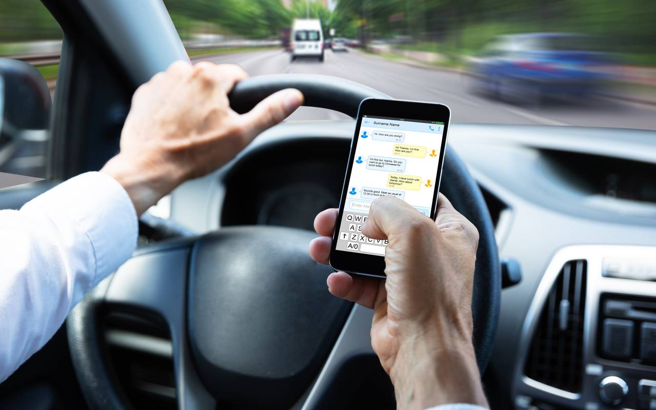 Mann tippt Textnachricht auf dem Handy, während er Auto fährt.