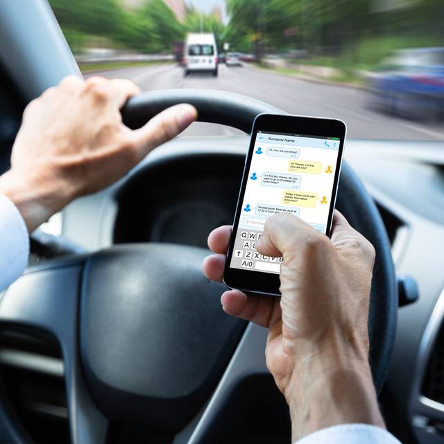 Mann tippt Textnachricht auf dem Handy, während er Auto fährt.