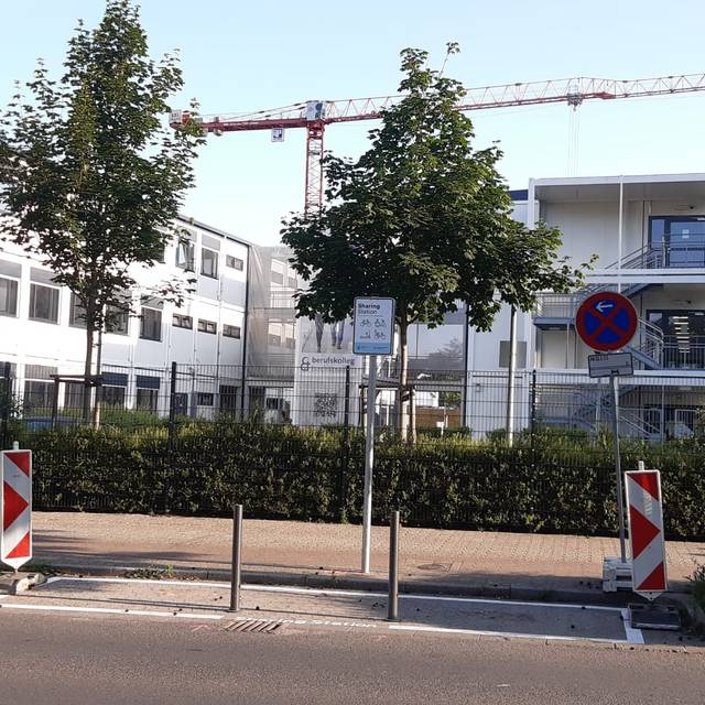 Im Vordergrund ein abgesperrter Parkplatz, an dem ein Schild mit der Info "Sharing-Station"