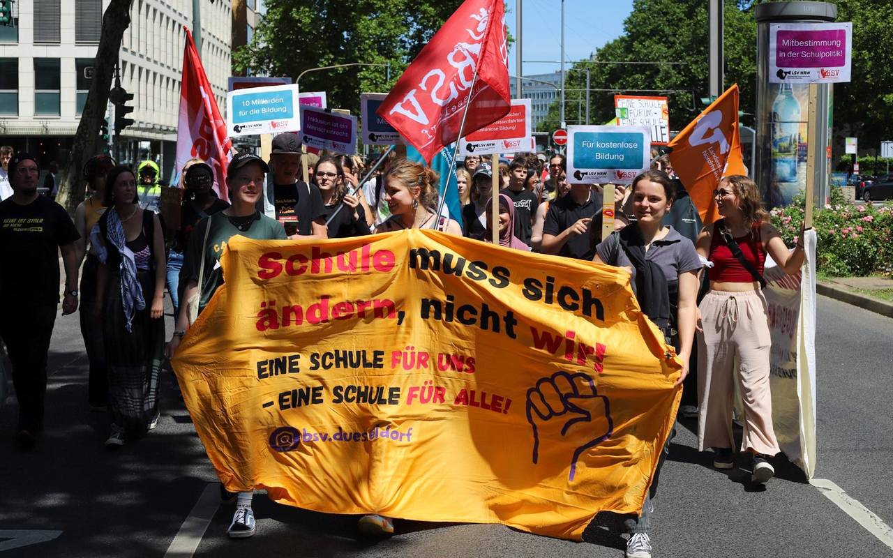 Eine Gruppe Schüler*innen demonstriert, indem sie ein Banner vor sich her trägt, im Hintergrund weitere Schilder. Die Gruppe läuft über eine Straße.