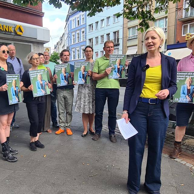 Eine Gruppe Menschen steht im Halbkreis um die Grünen-Politikerin Clara Gerlach, alle halten Schilder hoch.