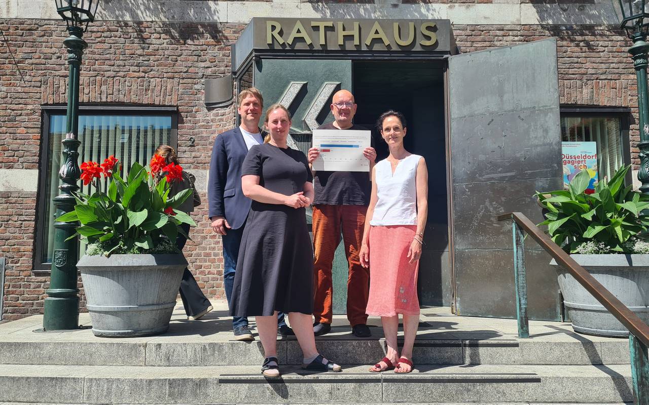 Vier Menschen stehen auf den Stufen vor der Eingangstür zum Düsseldorfer Rathaus. Einer hält ein Schild in den Händen.