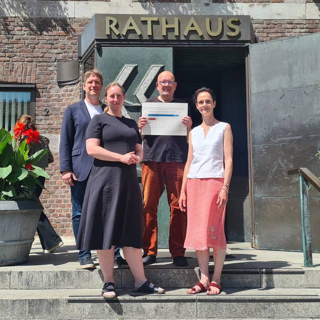 Vier Menschen stehen auf den Stufen vor der Eingangstür zum Düsseldorfer Rathaus. Einer hält ein Schild in den Händen.