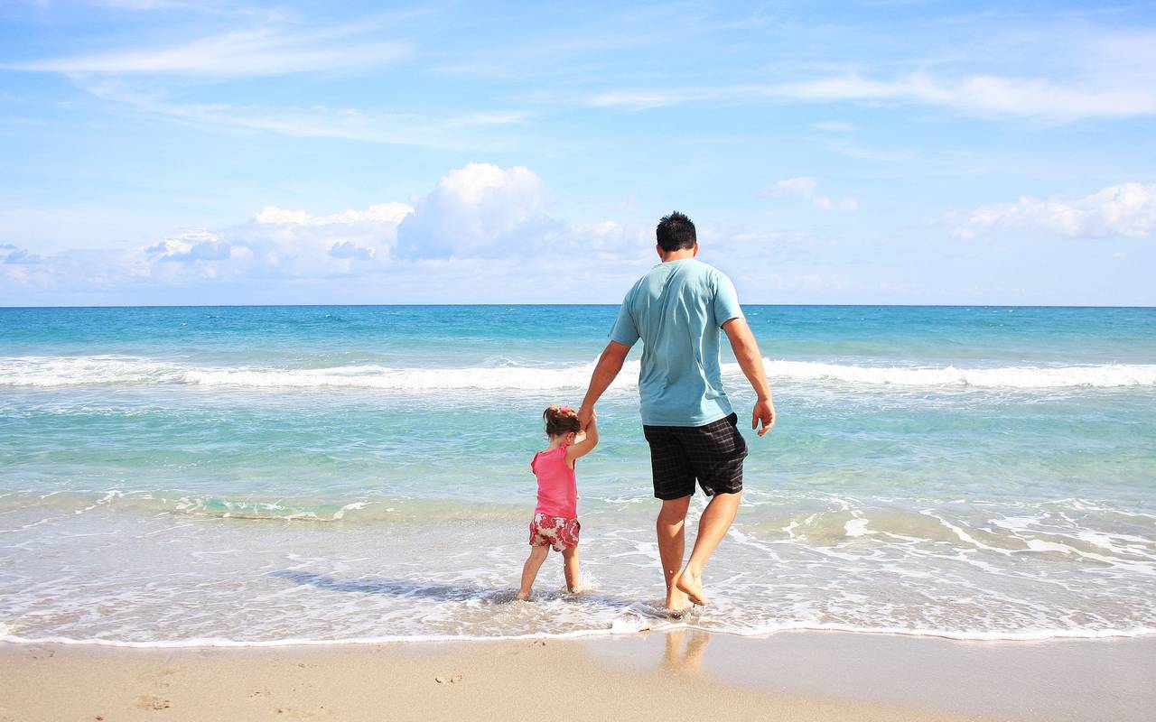 Vater und Kind gehen Hand in Hand im Sommer im seichten Wasser am Strand