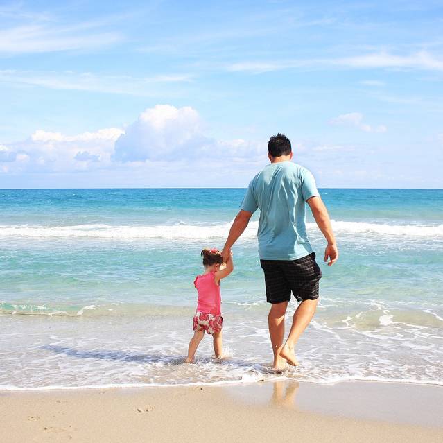 Vater und Kind gehen Hand in Hand im Sommer im seichten Wasser am Strand