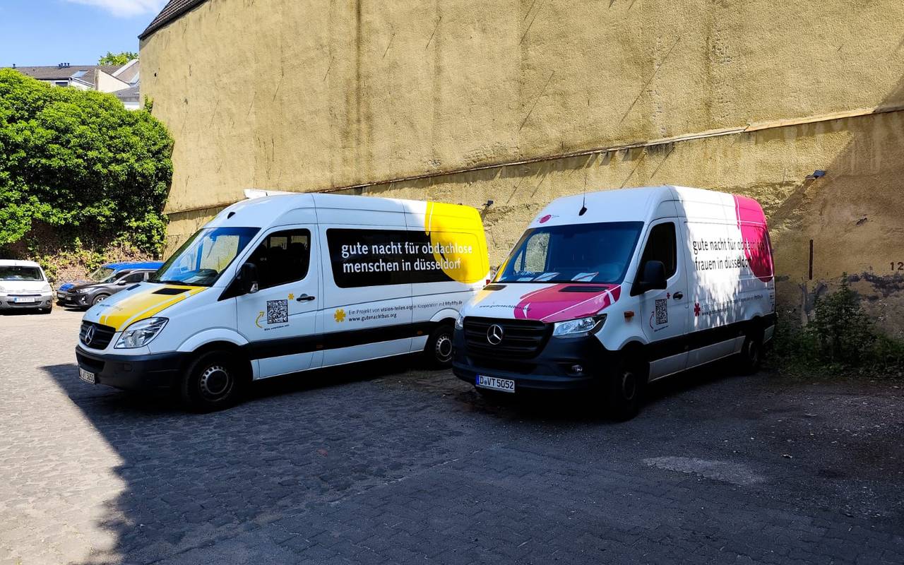Zwei Busse mit der Aufschrift "gute nacht für obdachlose menschen in düsseldorf" stehen vor einer Mauer