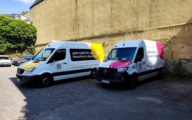 Zwei Busse mit der Aufschrift "gute nacht für obdachlose menschen in düsseldorf" stehen vor einer Mauer