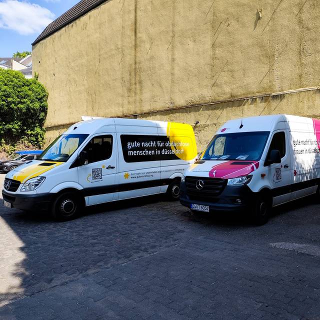 Zwei Busse mit der Aufschrift "gute nacht für obdachlose menschen in düsseldorf" stehen vor einer Mauer
