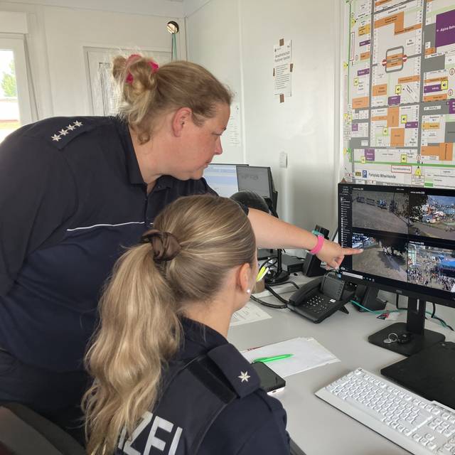 Zwei Polizistinnen schauen auf einen viergeteilten Bildschirm, der Bilder einer Überwachungskamera von der Düsseldorfer Rheinkirmes zeigt.