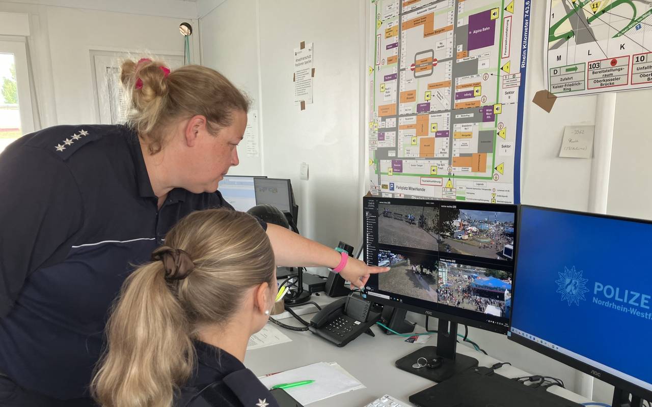 Zwei Polizistinnen schauen auf einen viergeteilten Bildschirm, der Bilder einer Überwachungskamera von der Düsseldorfer Rheinkirmes zeigt.