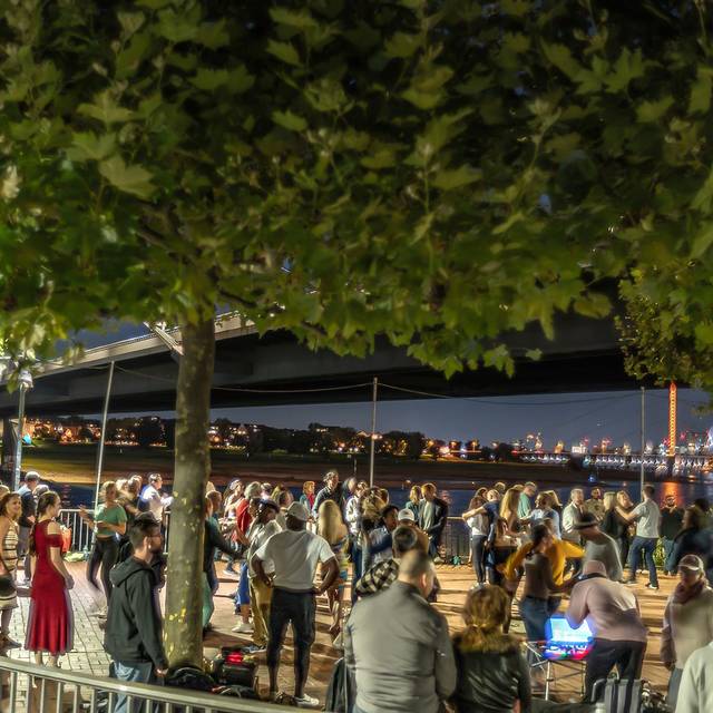 Viele Menschen tanzen in der Nähe der Kniebrücke Salsa unter freiem Himmel. Im Hintergrund sind die Lichter der Rheinkirmes zu sehen.