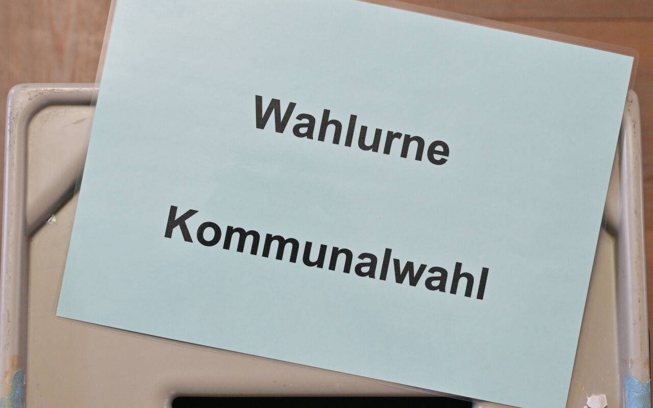 Ein Zettel mit der Aufschrift "Wahlurne Kommunalwahl" liegt auf einer Wahlurne in einem Wahllokal.