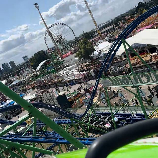 Blick von der Alpina-Achterbahn auf die Rheinkirmes. Im Vordergrund ein Wagen der Alpina-Bahn, im Hintergrund der Kirmesplatz mit Riesenrad und Rheinturm.