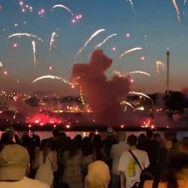 Mehrere Menschen stehen am Mannesmannufer und beobachten das Feuerwerk. Auf der anderen Rheinseite sieht man, wie ein Feuerwerkskörper sehr niedrig explodiert ist.