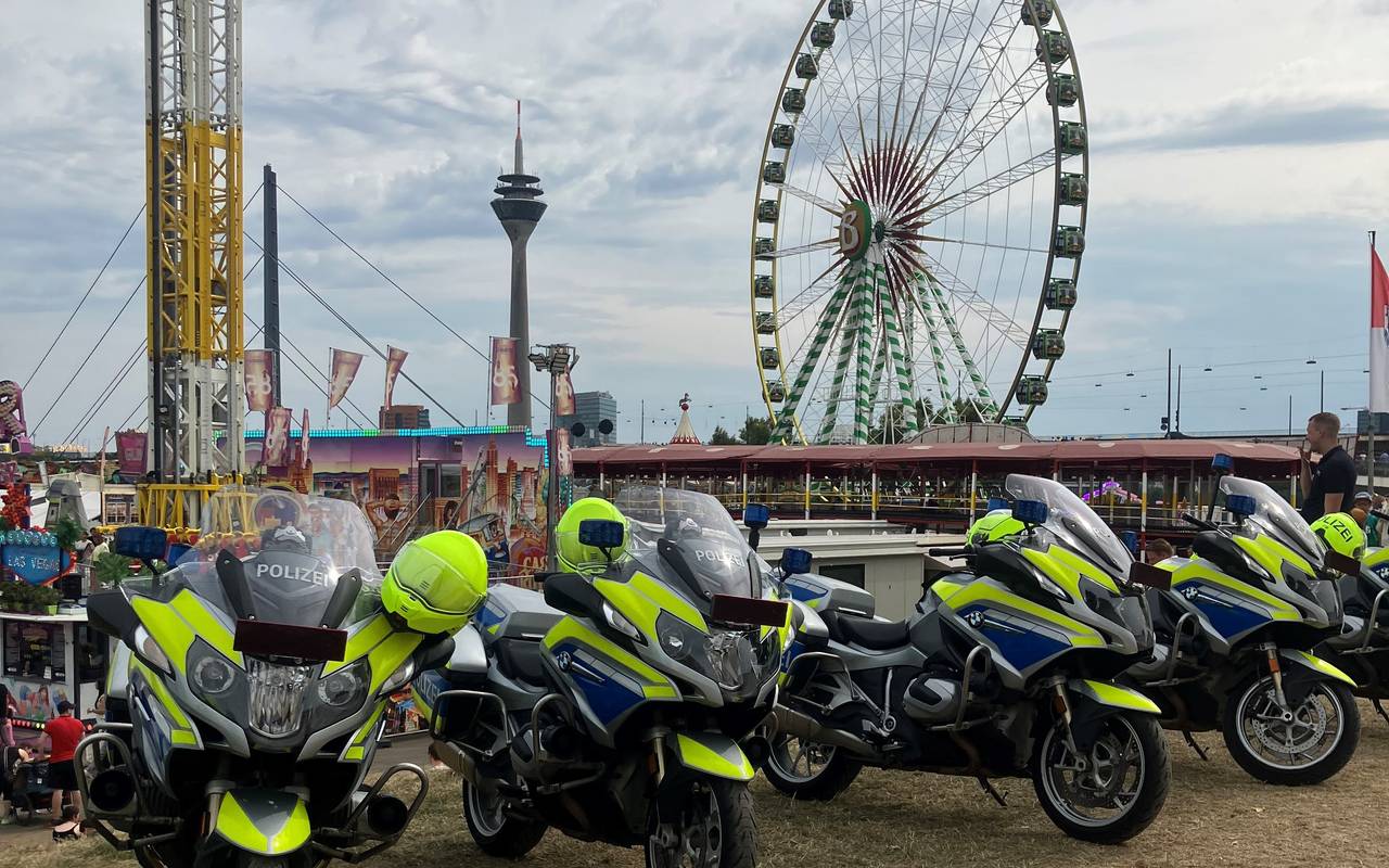 Motorräder der Polizei stehen aufgereiht am Rand der Rheinkirmes. Im Hintergrund der Kirmesplatz mit Riesenrad sowie der Rheinturm.