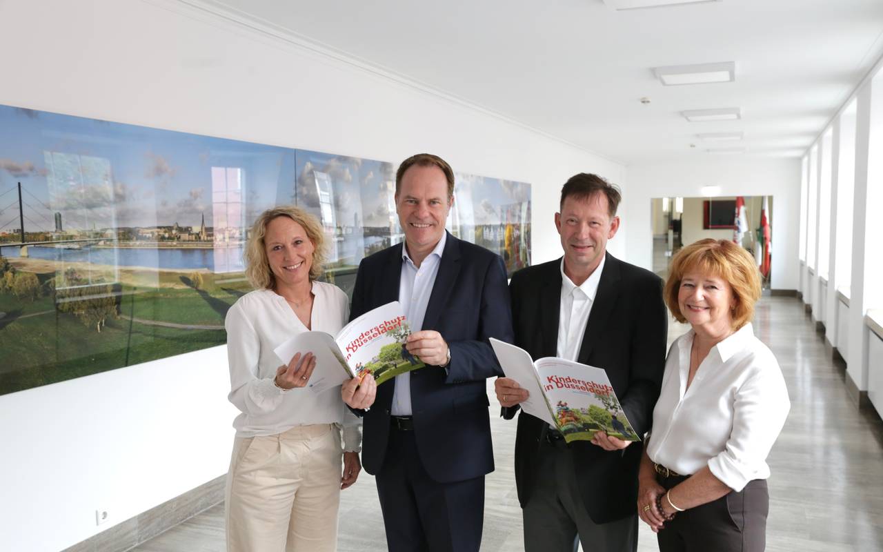 Daniela Schmitt, Sachgebietsleitung 24-Stunden Kinderschutzdienst, Oberbürgermeister Dr. Stephan Keller, Stadtdirektor Burkhard Hintzsche, und Renate Schäfer-Sikora, stellvertretende Leiterin des Amtes für Soziales und Jugend stehen im Rathaus und halten die neue Broschüre "Kinderschutz in Düsseldorf" in der Hand.