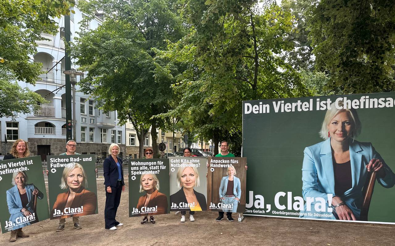 Oberbürgermeister-Kandidatin Clara Gerlach steht zwischen ihren Wahlplakaten, auf denen jeweils Clara Gerlach zu sehen ist. Daneben ein Großplakat der Kampagne.