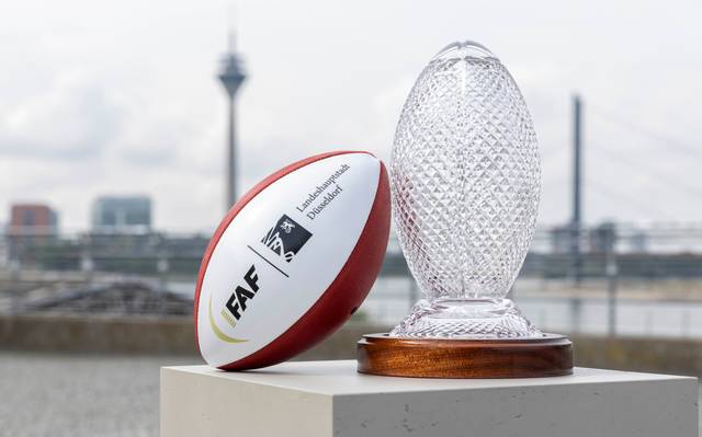 Ein Football und der Pokal der Flag Football WM stehen auf dem Burgplatz. Im Hintergrund sind die Rheinkniebrücke und der Rheinturm.