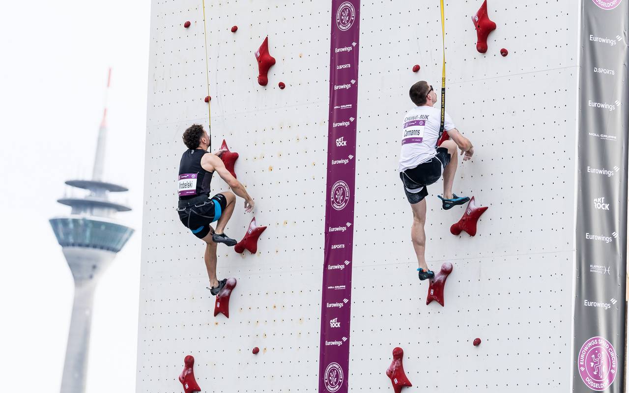 Zwei Speedkletterer klettern eine Kletternwand hoch, im Hintergrund der Rheinturm