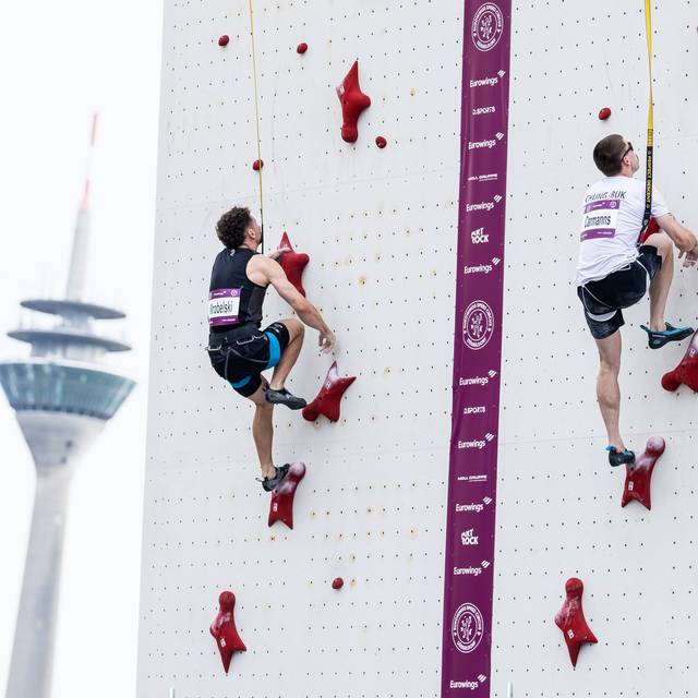 Zwei Speedkletterer klettern eine Kletternwand hoch, im Hintergrund der Rheinturm
