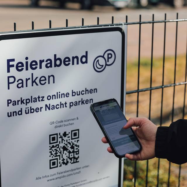 Mit seinem Smartphone in der hand scannt ein Mann den QR-Code auf dem Schild für das Feierabend-Parken.