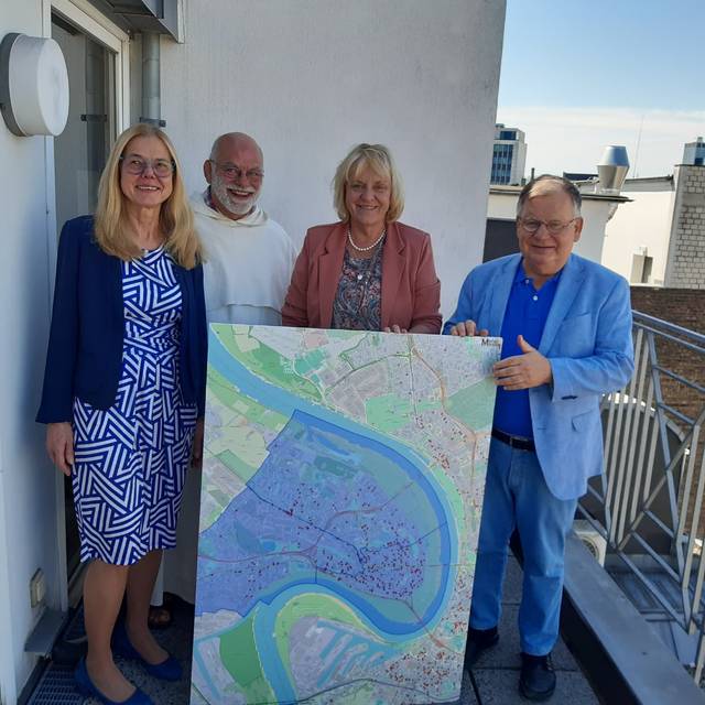 Zwei Frauen und zwei Männer stehen auf einer Dachterrasse, hinter einer Karte von Düsseldorf mit roten Punkten.