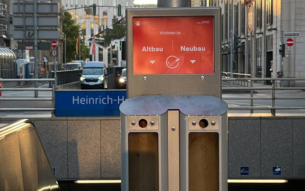 Abstimm-Aschenbecher am Eingang zur U-Bahnstation Heinrich-Heine-Allee. Im Hintergrund Hochhäuser und die Straße in Richtung Könisallee.