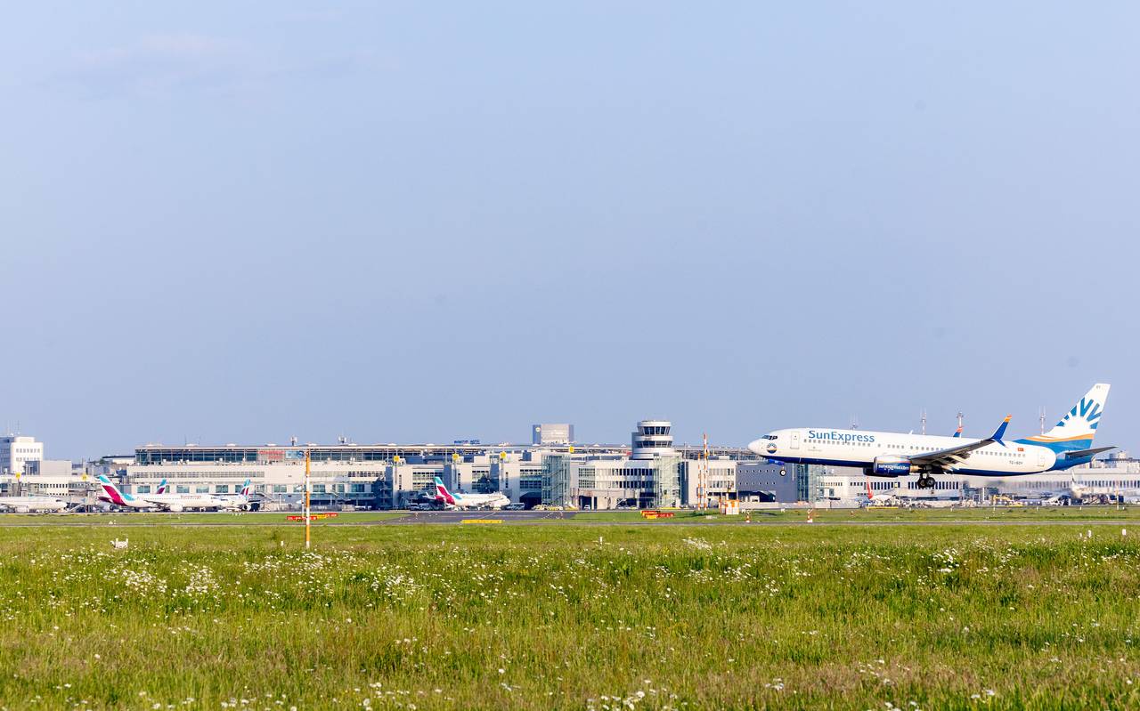 Rechts im Bild ein Flugzeug auf der Startbahn, das gerade abhebt, davor Rasen. Im Hintergrund der Düsseldorfer Flughafen, davor stehen einige Flugzeuge.