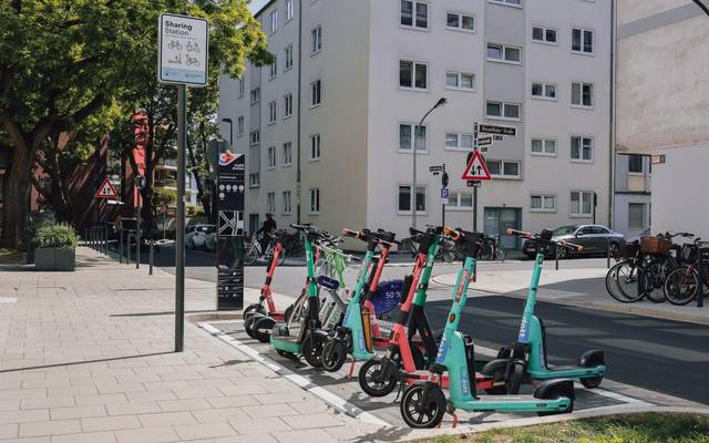 Ein paar Leihroller stehen an einer Mobilitätsstation in Düsseldorf. Im Hintergrund sind eine Straße und Hochhäuser