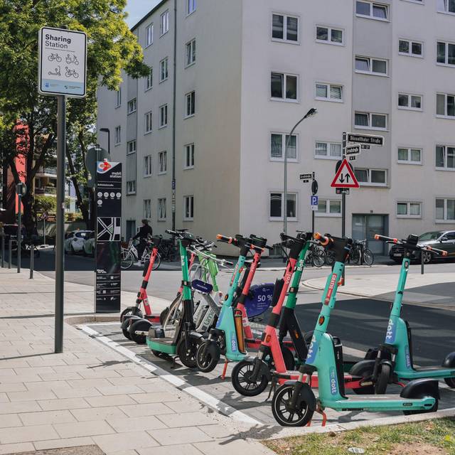 Ein paar Leihroller stehen an einer Mobilitätsstation in Düsseldorf. Im Hintergrund sind eine Straße und Hochhäuser