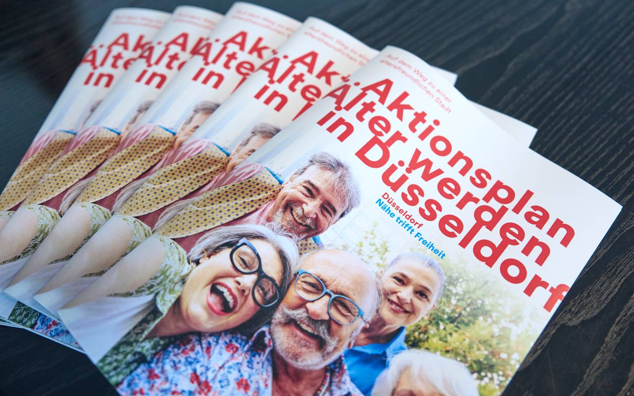 Mehrere Broschüren vom Aktionsplan "Älter werden in Düsseldorf" liegen auf einem Tisch.