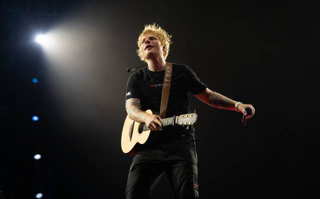 Ed Sheeran performet auf einer Bühne. Dabei wird er von einem Scheinwerfer angeleuchtet.