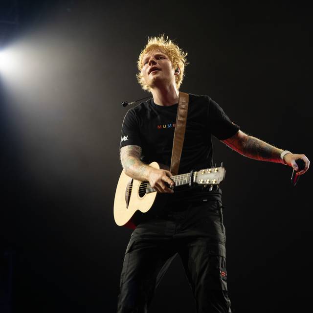 Ed Sheeran performet auf einer Bühne. Dabei wird er von einem Scheinwerfer angeleuchtet.