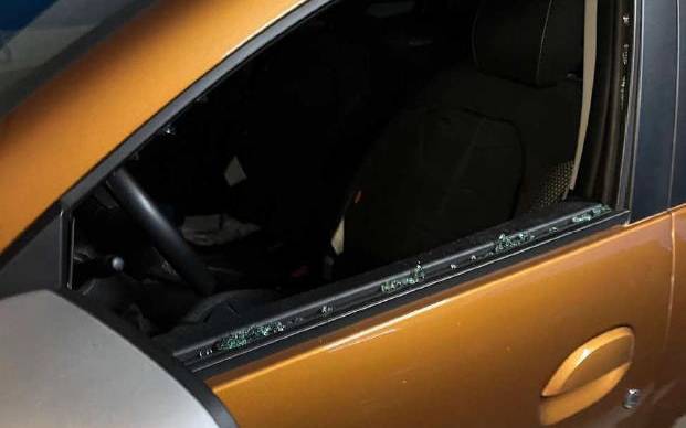 Fahrertür mit eingeschlagenem Autofenster eines ockerfarbenen Dacia. Einzelne Glassplitter der Scheibe sind im Türrahmen neben dem Außenspiegel zusehen.
