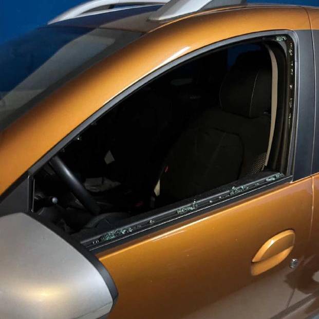 Fahrertür mit eingeschlagenem Autofenster eines ockerfarbenen Dacia. Einzelne Glassplitter der Scheibe sind im Türrahmen neben dem Außenspiegel zusehen.