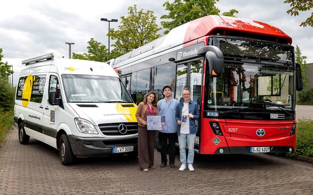 Vor einem weißen Kleinbus und einem roten Linienbus stehen drei Menschen und lächeln.