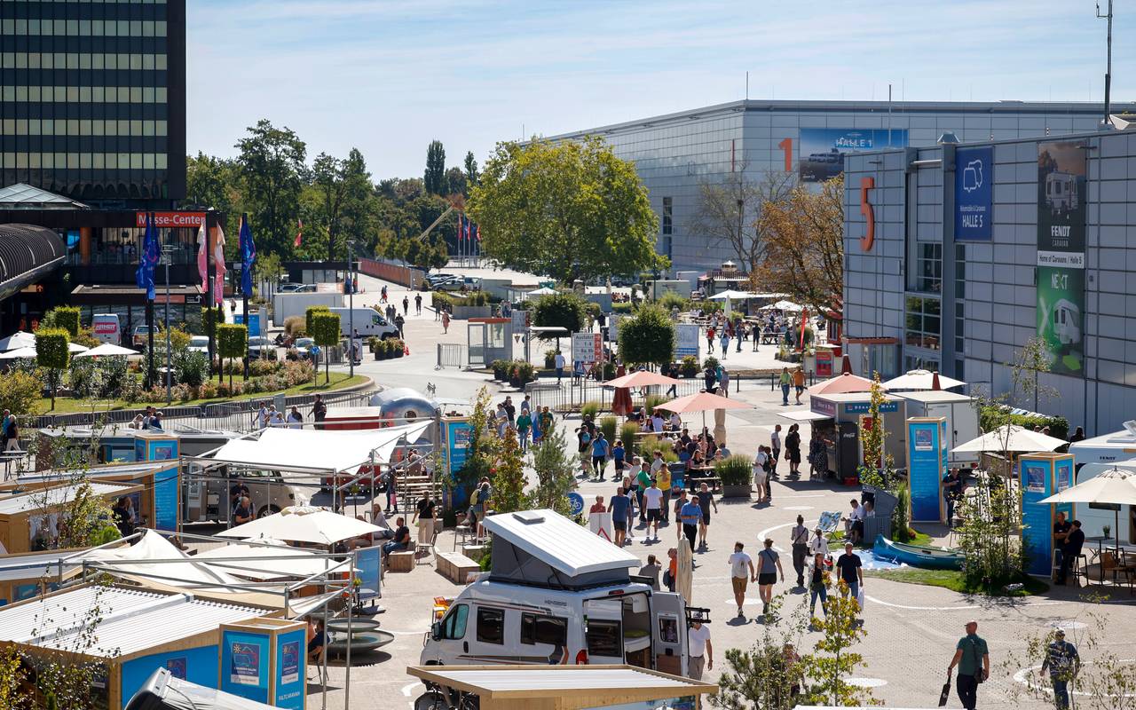 Ein Parkplatz mit Gastro-Zelten und Caravans. Zwischen den Ständen laufen Menschen hin und her.