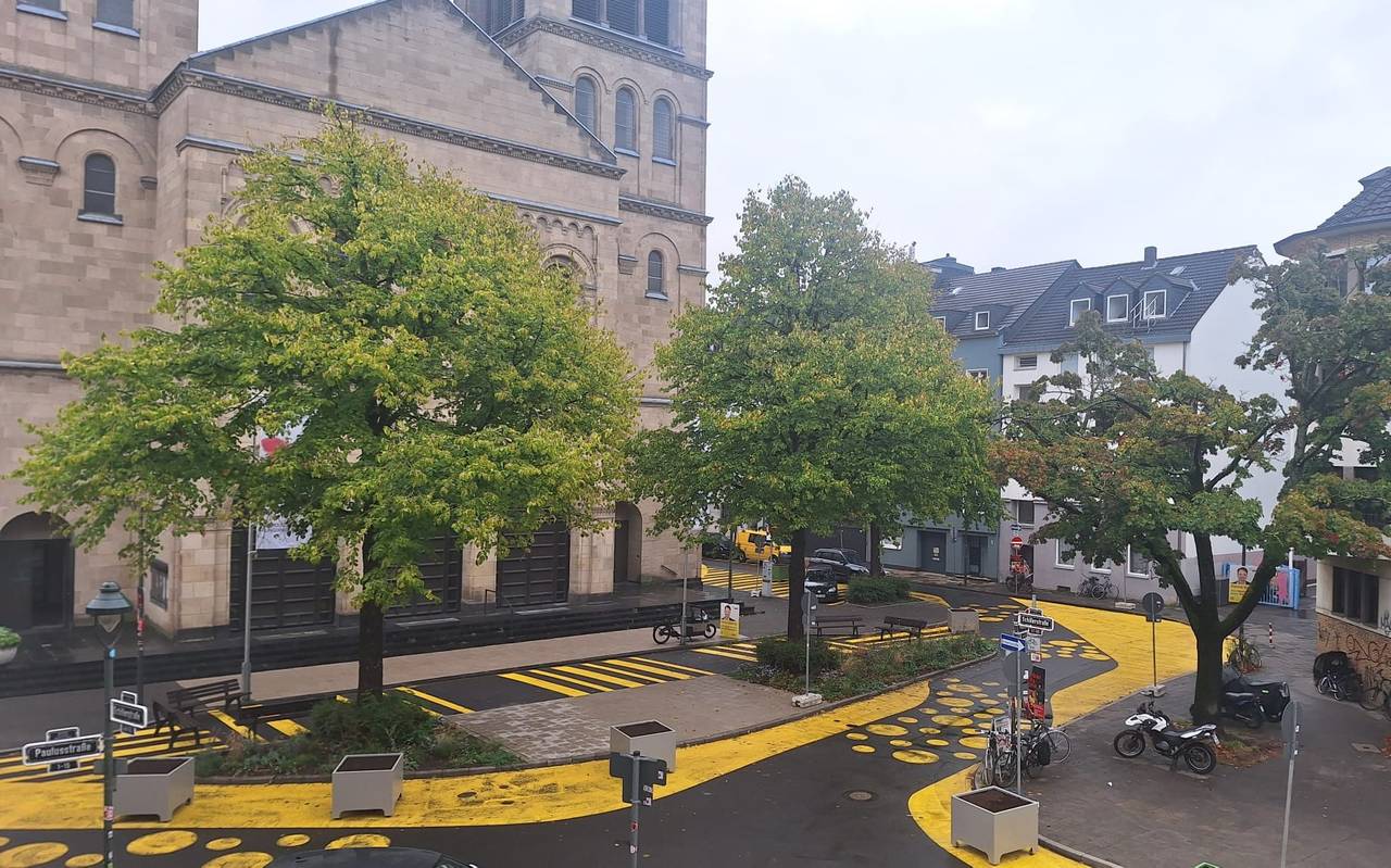 Auf dem Bild sieht man den Paulusplatz mit gelben Streifen und Punkten auf der Straße. Zusätzlich hat die Stadt Blumenkübel aufgestellt.
