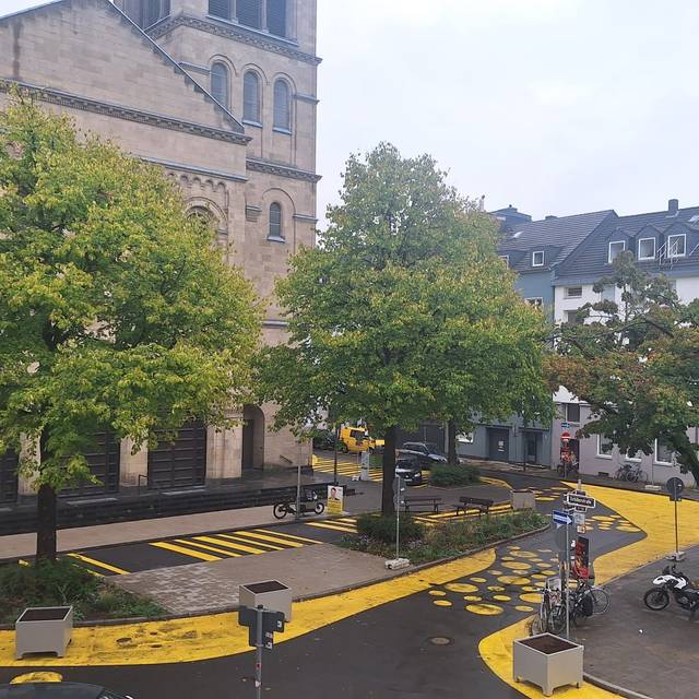 Auf dem Bild sieht man den Paulusplatz mit gelben Streifen und Punkten auf der Straße. Zusätzlich hat die Stadt Blumenkübel aufgestellt.