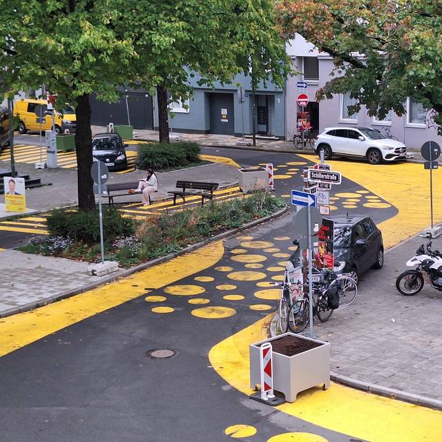 Auf dem Bild sieht man den Paulusplatz mit gelben Streifen und Punkten auf der Straße. Zusätzlich hat die Stadt Blumenkübel und Warnbaken aufgestellt.