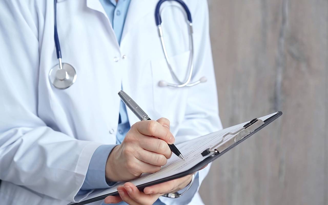 Weibliche Ärztin schreibt medizinische Unterlagen auf ein Klemmbrett, Gesicht nicht erkennbar, Symbolbild für Medizin und Pharmazie.