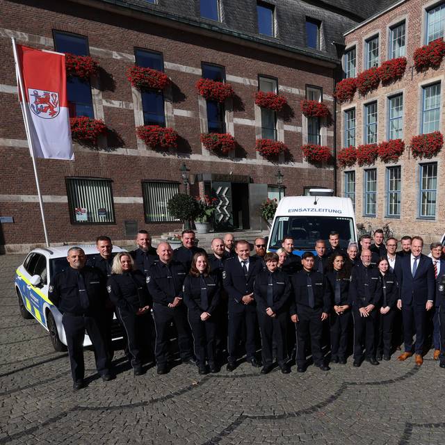 Über 50 neue OSD-Mitarbeitende stehen aufgereiht vor dem Düsseldorfer Rathaus. Hinter der Gruppe parken Autos des OSD. Vor dem Rathaus weht die Düsseldorf-Flagge.