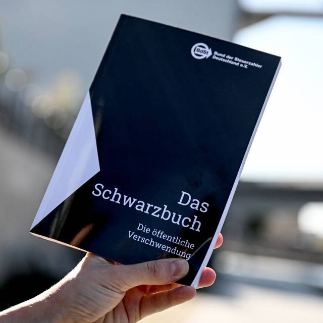 Das Schwarzbuch 2025/26 vom Bund der Steuerzahler in wird vor das Reichstagsgebäude gehalten. Das Schwarzbuch listet Beispiele auf, wo aus Sicht des Steuerzahlerbunds Steuergelder verschwendet wurden.