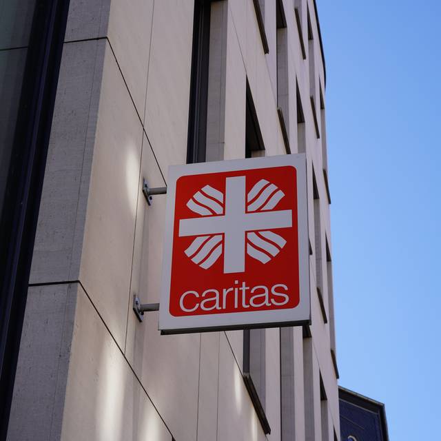 Ein Schild der Caritas hängt an einer Häuserwand. Dieses Bild dient als Symbolbild für die Caritas.